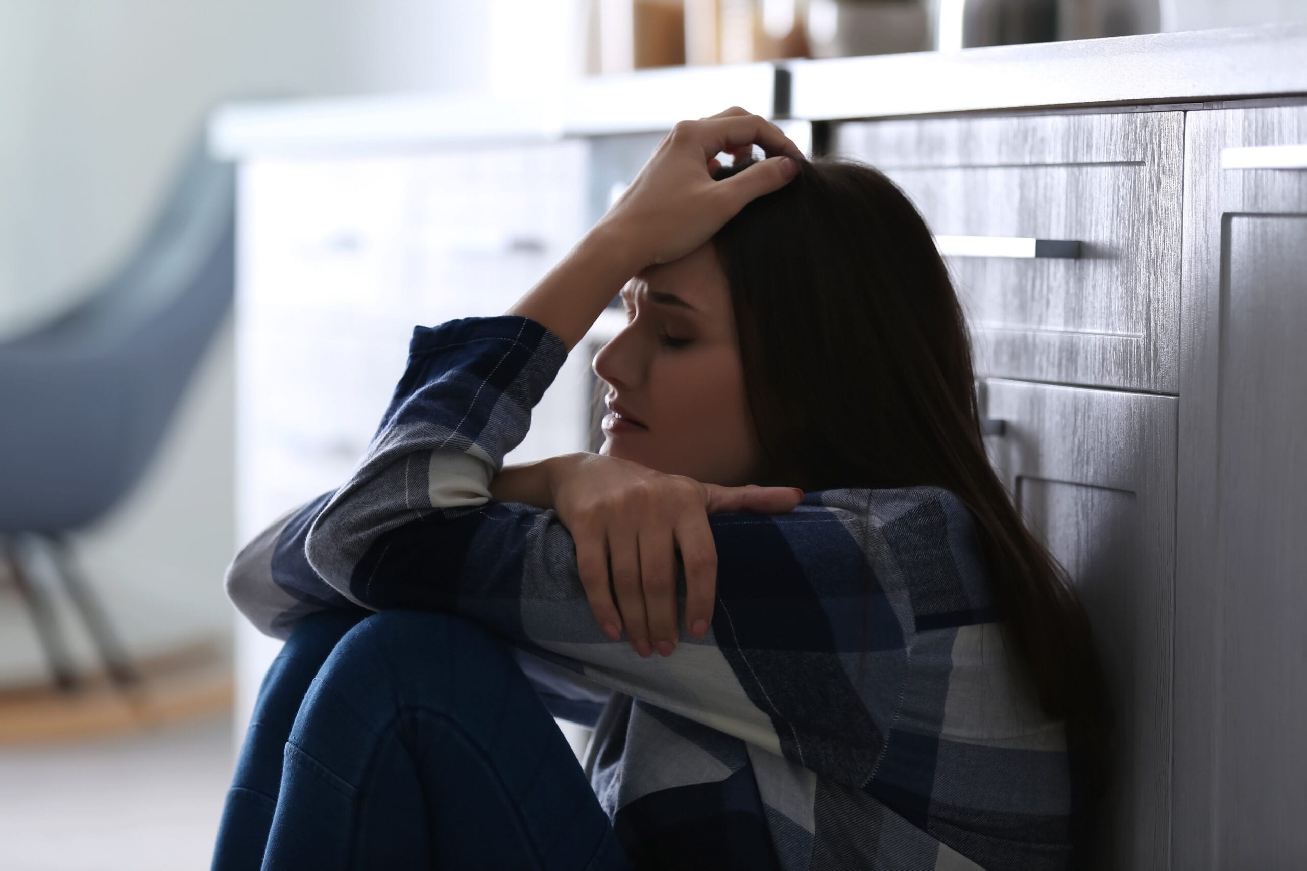 Mujer sentada en el suelo con la mano en la cabeza, mostrando ansiedad, agotamiento emocional y síntomas físicos de estrés.